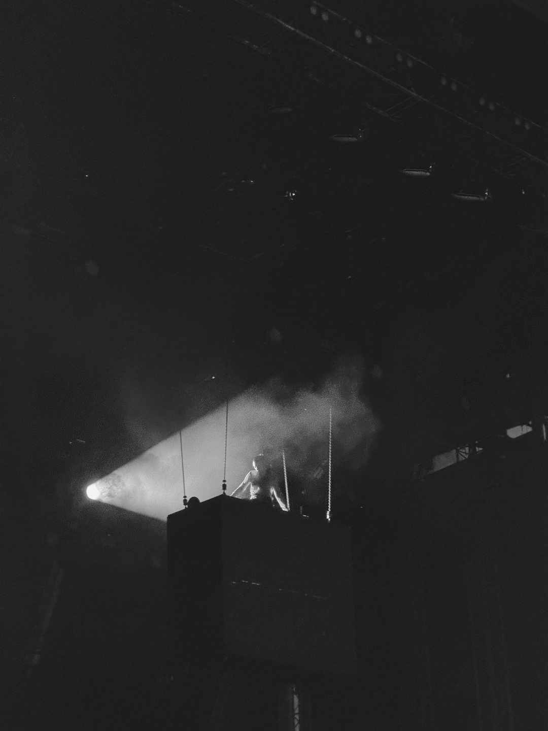 A dark, moody shot of Lorde on a suspended stage, with a beam of light cutting through the haze and silhouetting her.