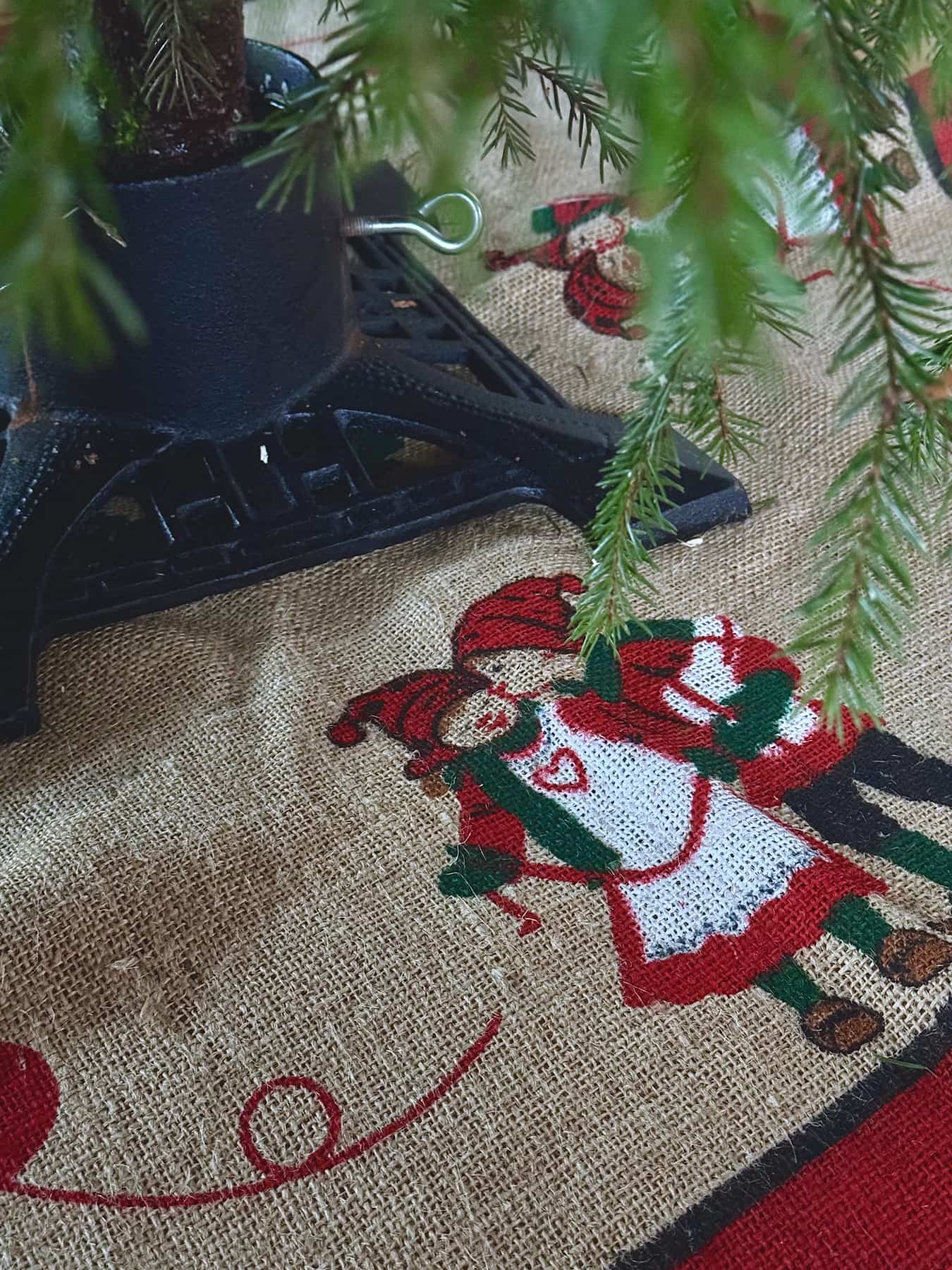 It&rsquo;s in an iron stand on a jute mat. The mat has an illustration of a boy kissing a girl, both dressed in festive holiday outfits.