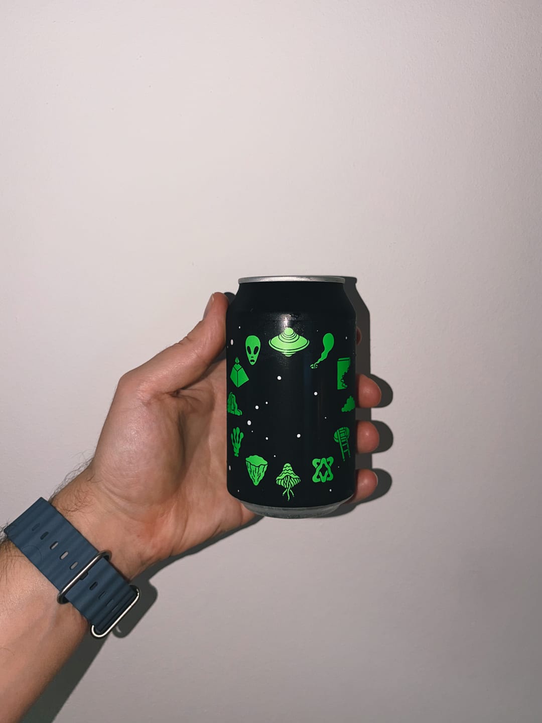 My hand holding a black can covered with cute green alien doodles.