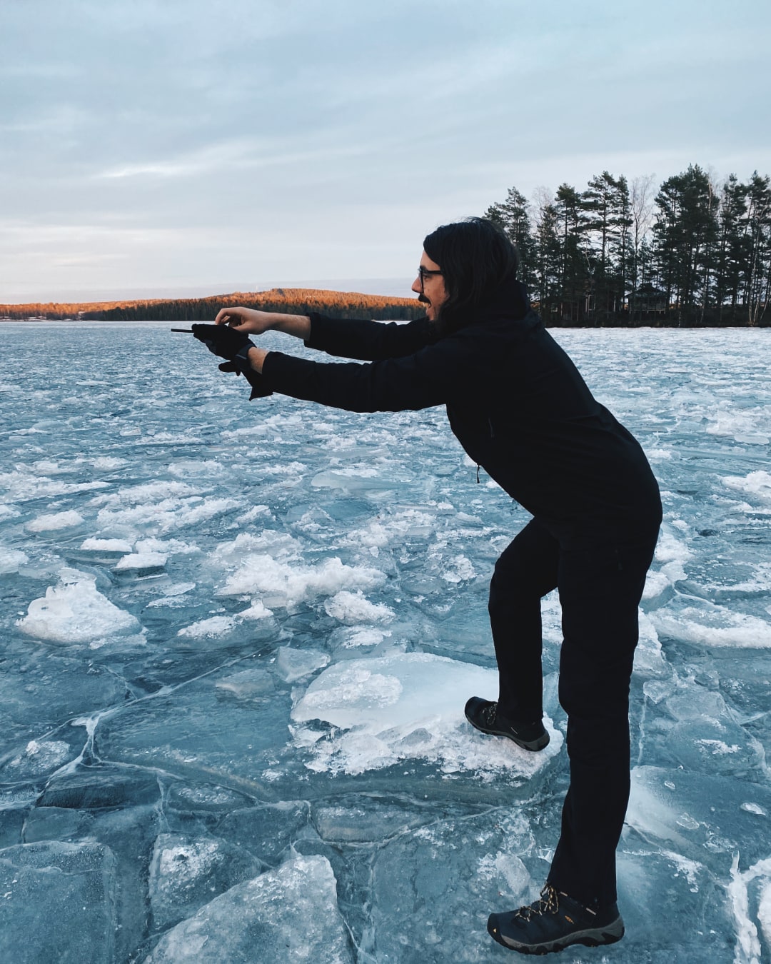 A man is standing on a frozen lake. He’s holding a smartphone far away from his body in an awkward position. He’s probably about to take a picture.