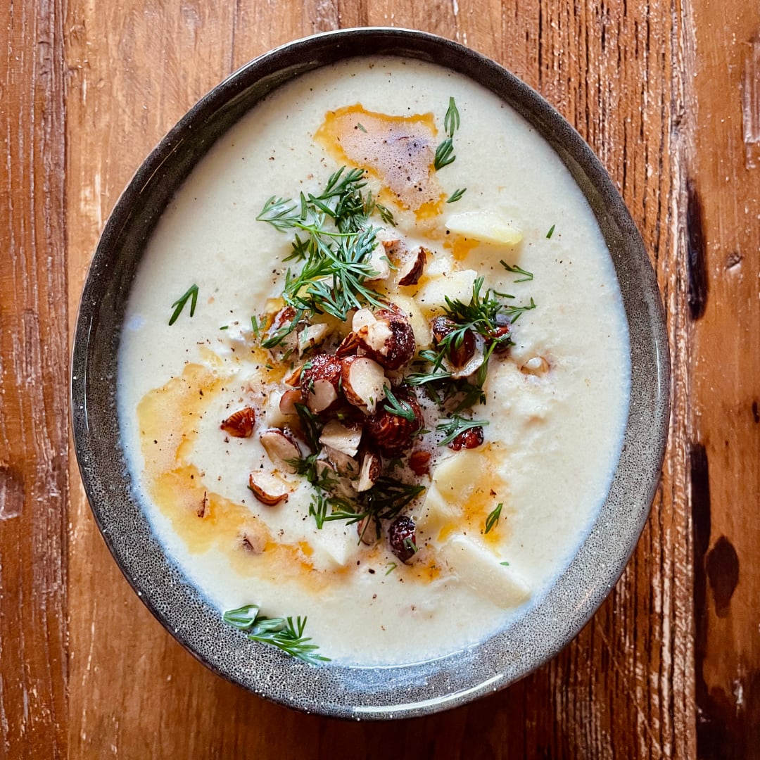Soup in an egg-shaped bowl. Topped with browned butter, dill, and hazelnuts.