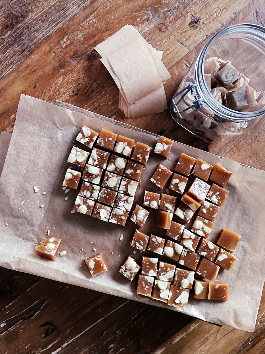 Chopped up pieces of caramel candy, laying on baking paper. There’s also a glass jar with wrapped candies and wrapping paper.