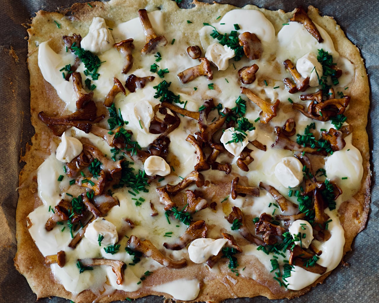 A pizza topped with chanterelle, cheese, mayo, and chive.
