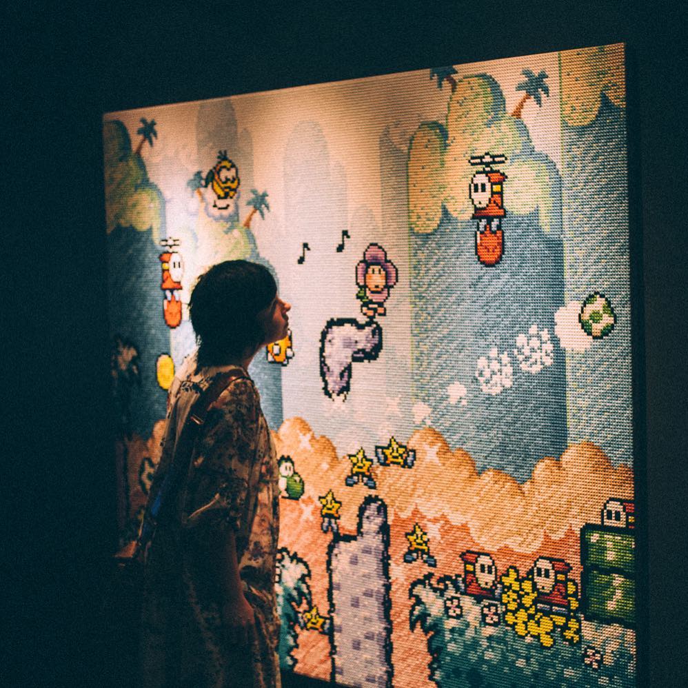 A woman is studying a huge, crossed stitched screenshot from the game Yoshi's Island.