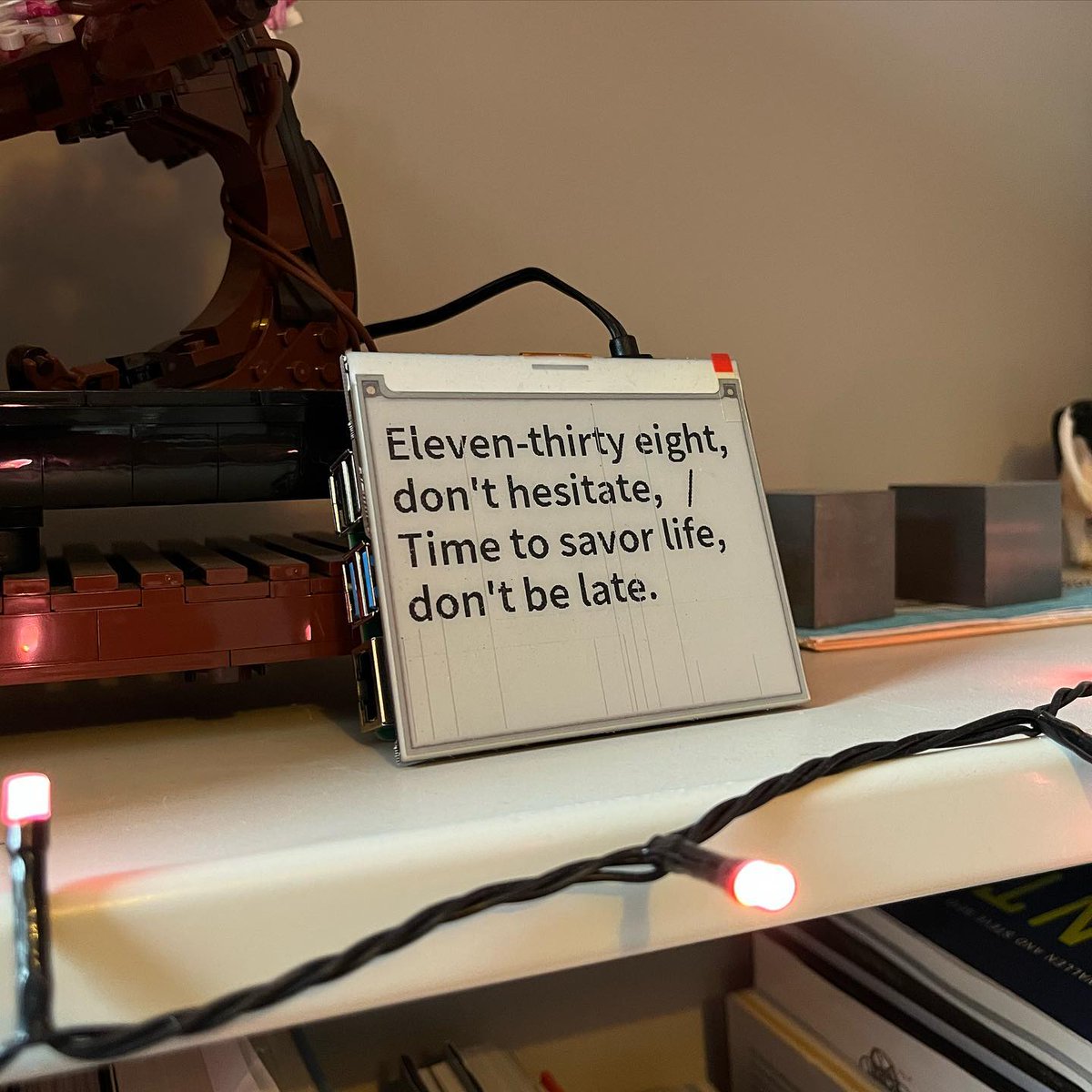 An e-ink screen on a shelf with the text: eleven-thirty eight, don't hesitate, Time to savor life, don't be late.