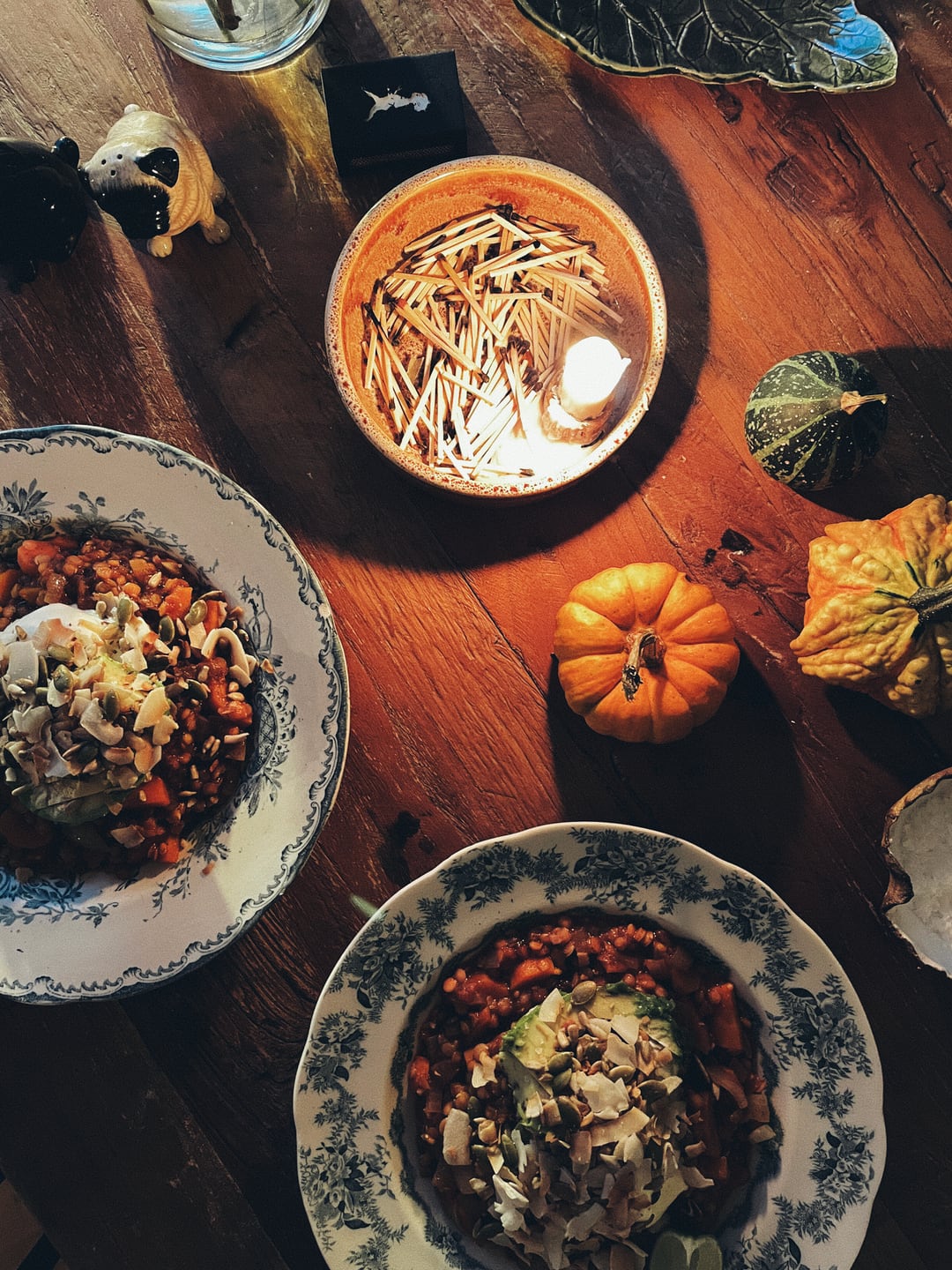 A table with two plates of dal, mini pumpkins, and a lit candle.