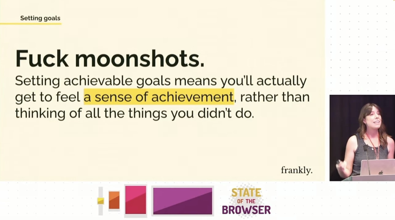Slide from the presentation with Amy standing on scene. Setting goals – fuck moonshots. Setting achievable goals means you'll actually get to feel a sense of achievement, rather than thinking of all the things you didn't do.
