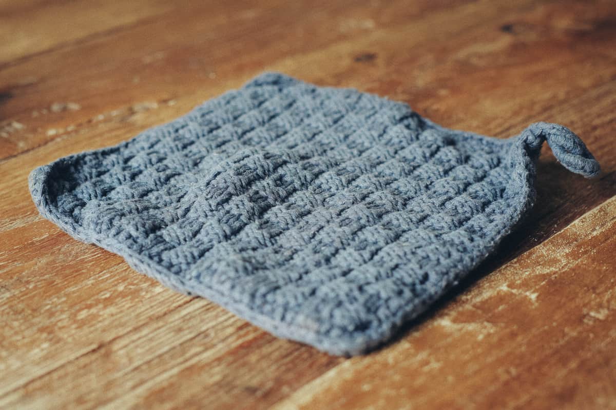A close-up of a slate gray handcrafted potholder with intricate textures resting atop a wooden table.