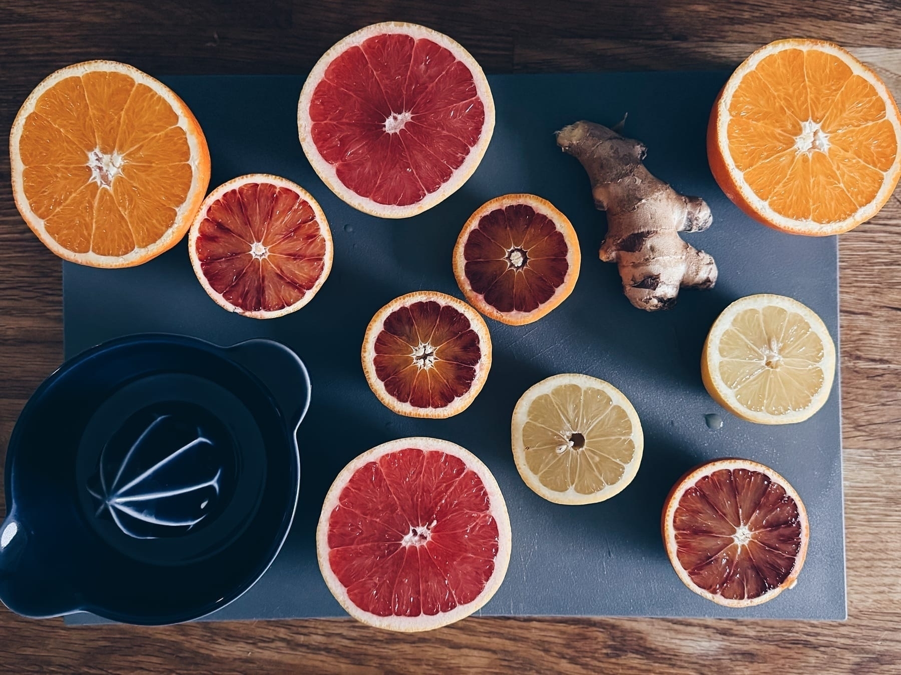 Sliced oranges, blood oranges, lemons, and a ginger on a cutting board with a juicer.