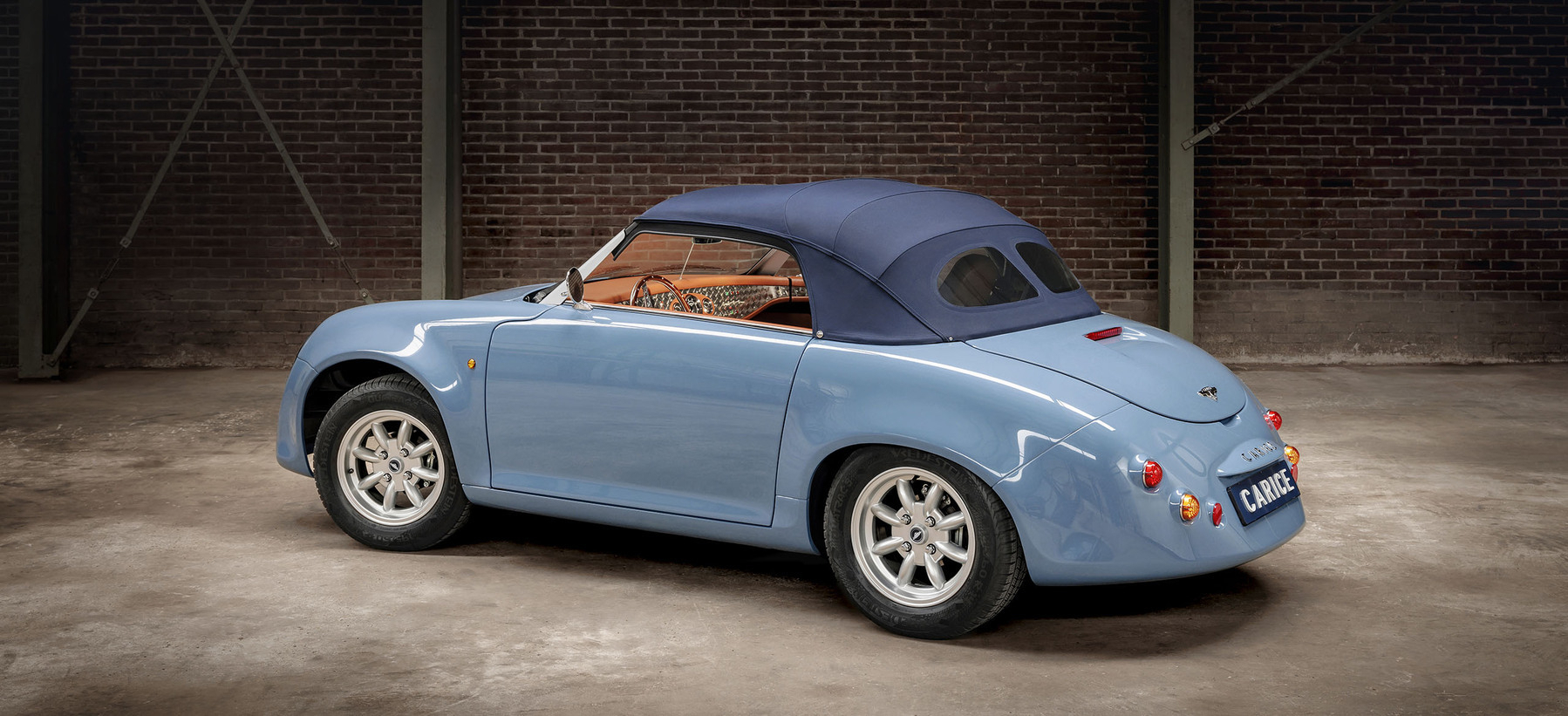A blue convertible car with a navy soft top parked in a spacious industrial-style garage with a brick wall background